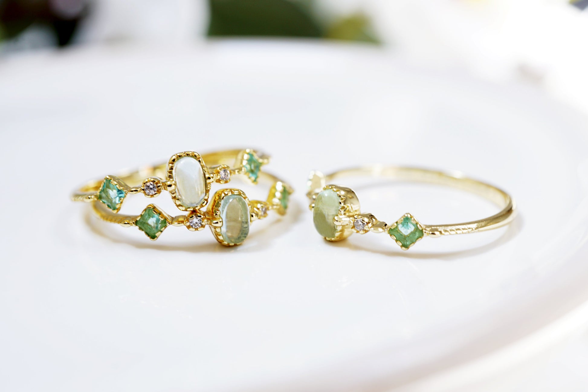 Two gold rings with green gemstones on a white surface