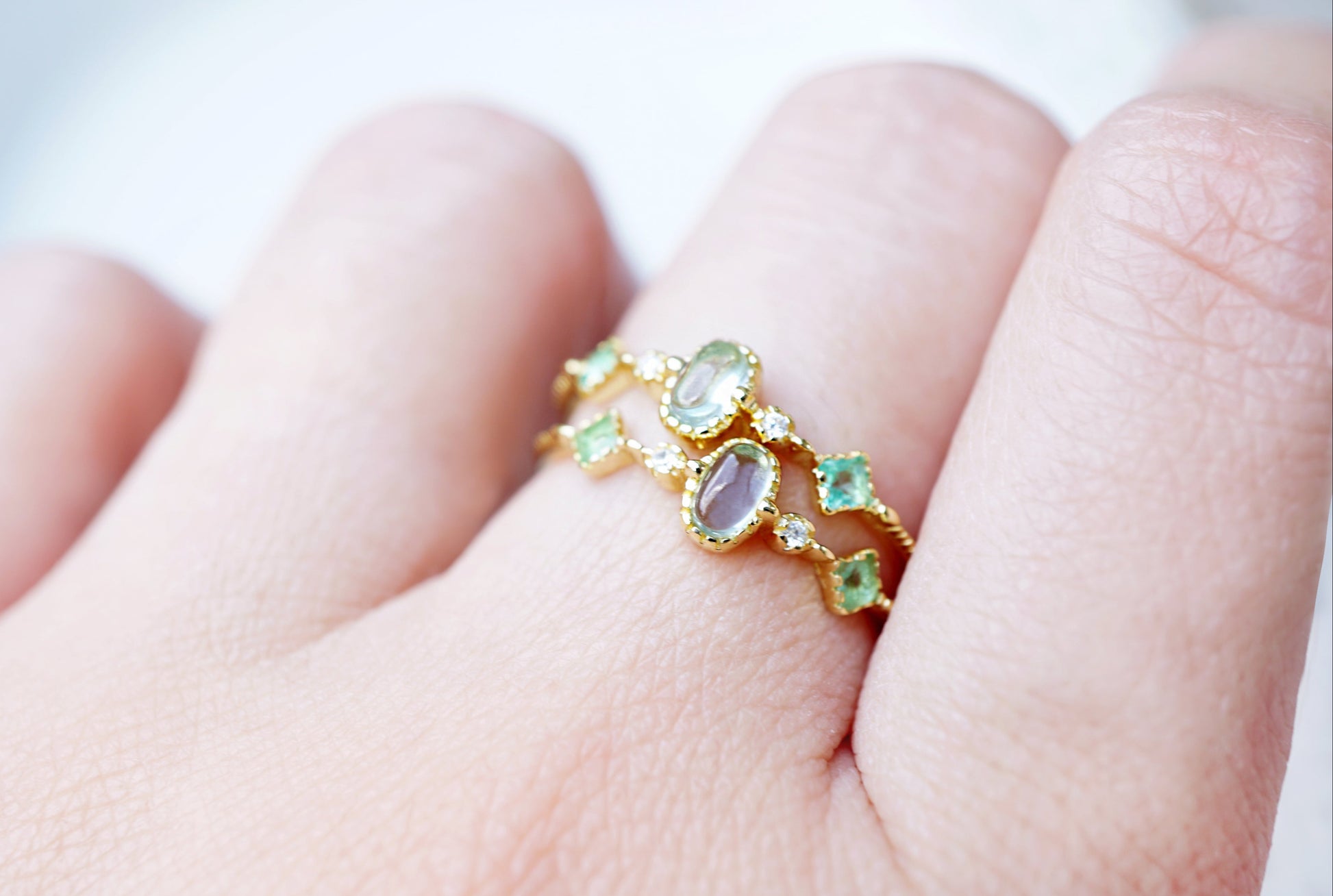 Gold ring with green gemstones on a finger against a blurred background