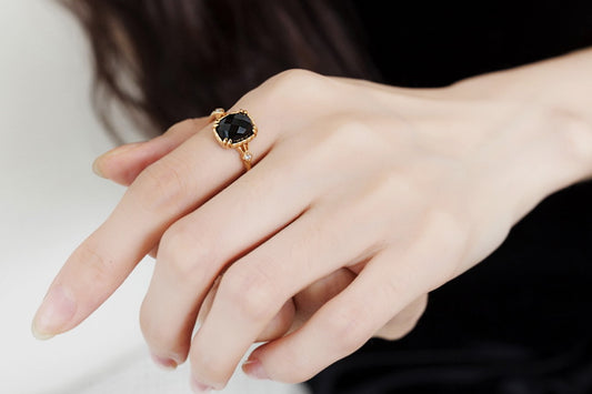 Close-up of a hand wearing a gold ring with a black gemstone.