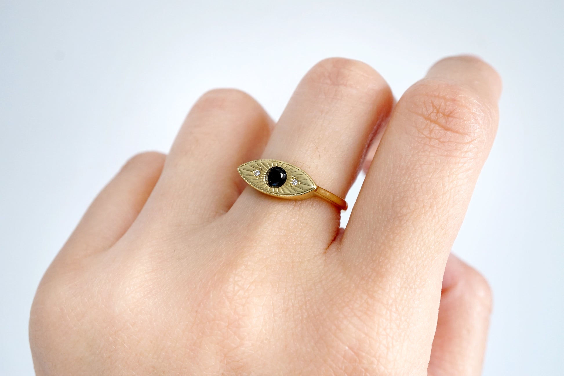 Gold ring with a black gemstone on a finger against a white background
