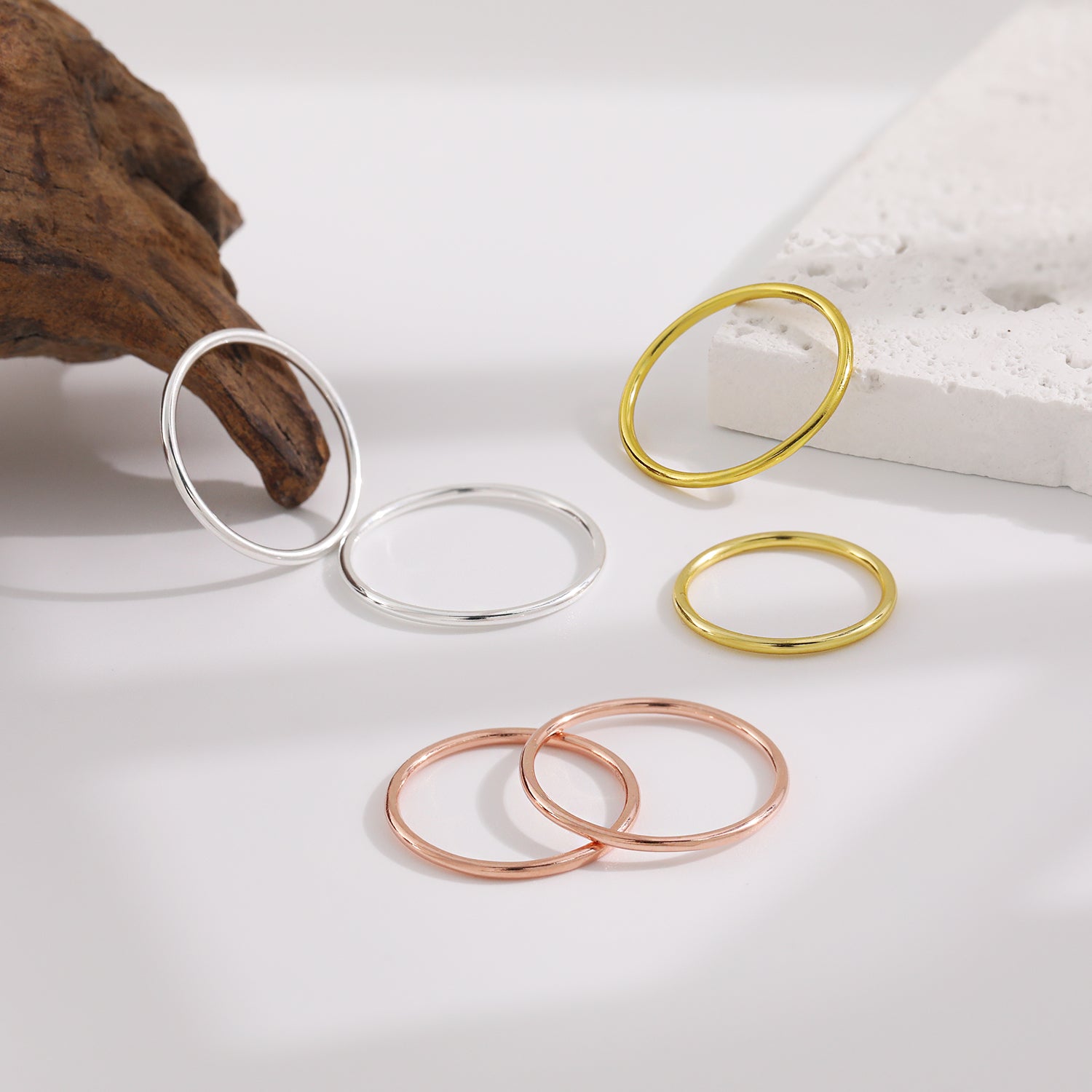 Three rings in silver, gold, and rose gold on a white surface with a wooden object in the background.