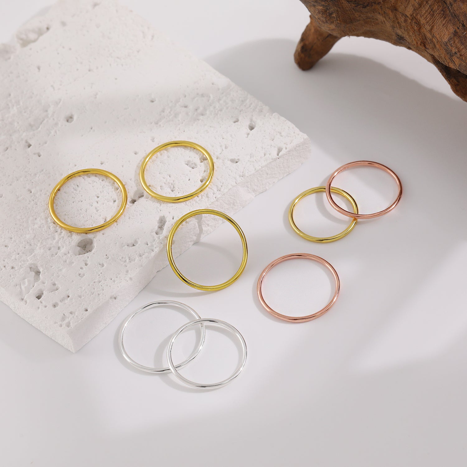 Set of gold, silver, and rose gold rings on a textured surface with a wooden block.