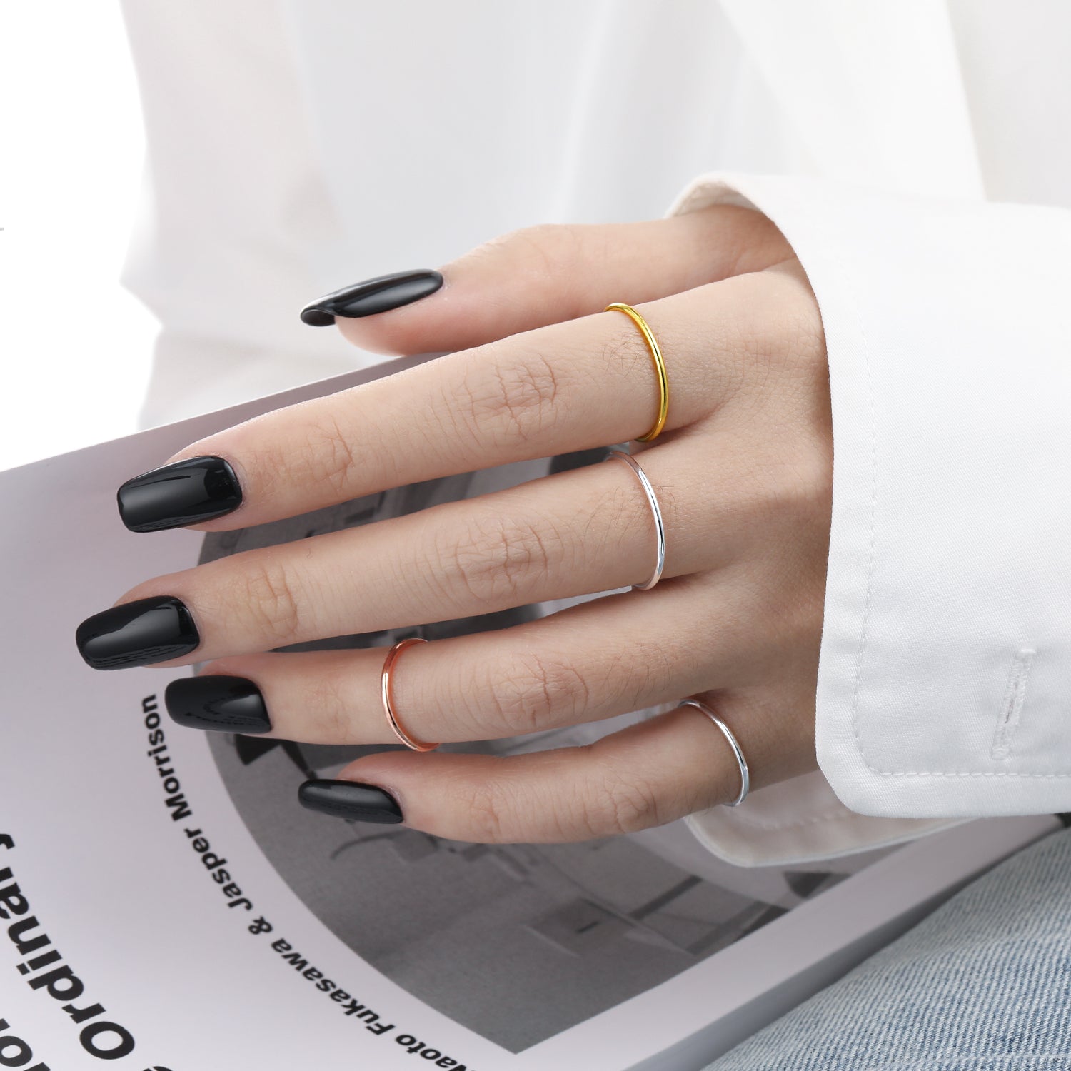 Hand with black nail polish wearing multiple rings on a magazine background