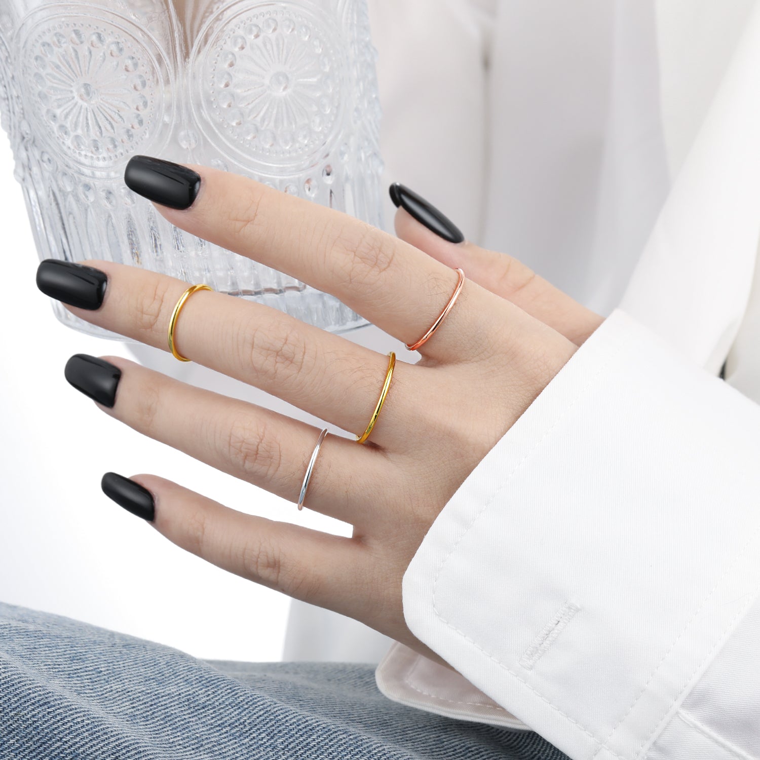 Hand wearing multiple rings with black nail polish on a white background