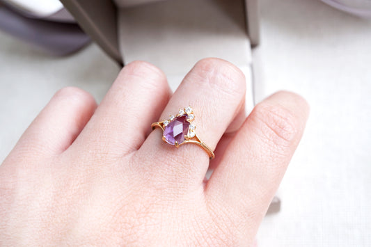 Hand wearing a gold ring with an amethyst stone on a blurred background