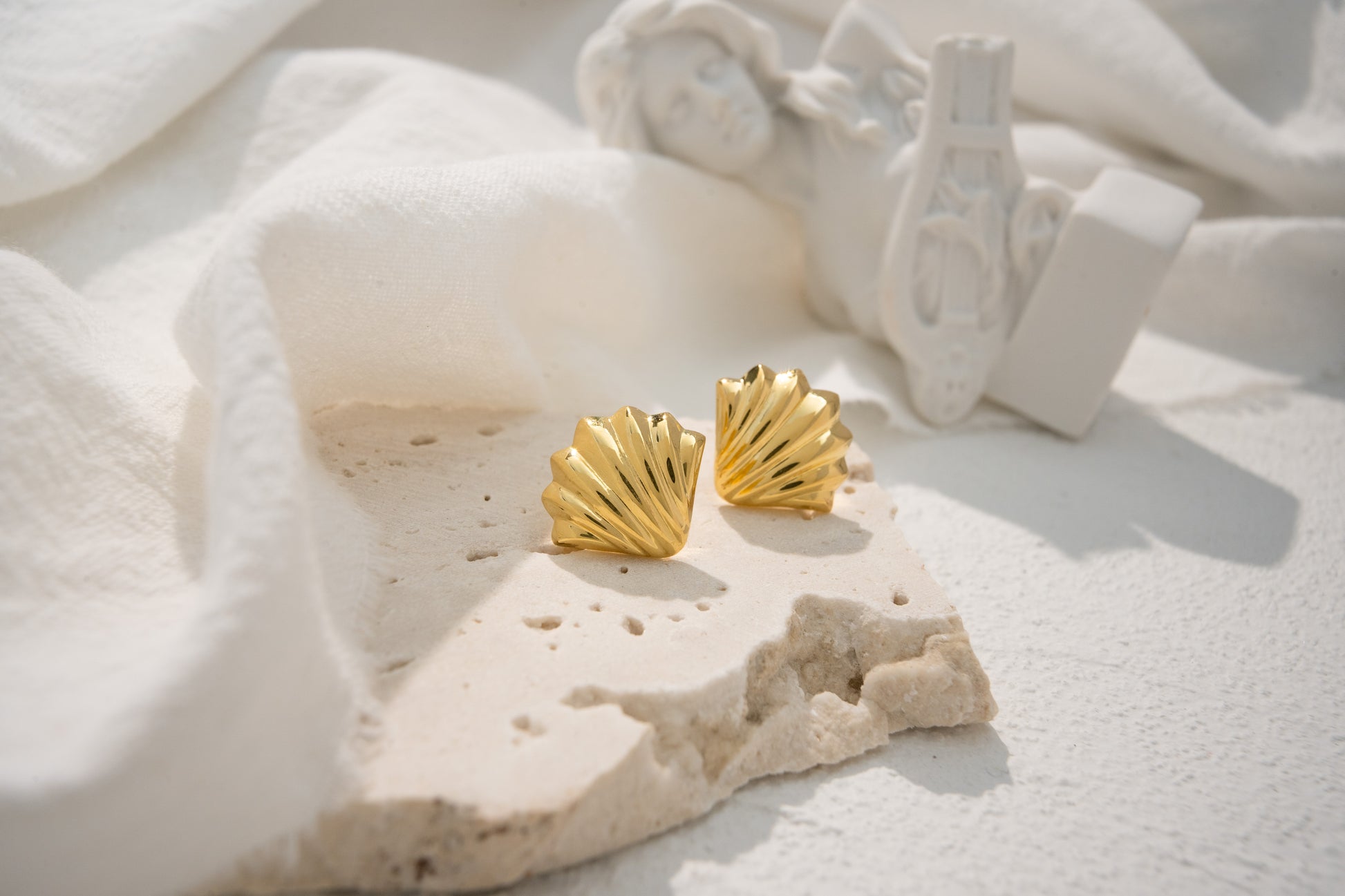 Shell-shaped earrings in gold and silver on a textured stone surface.