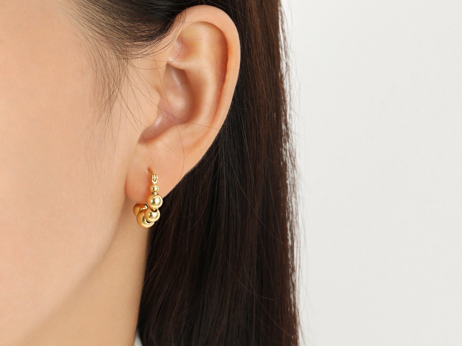 Gold hoop earrings worn by a person with a neutral background