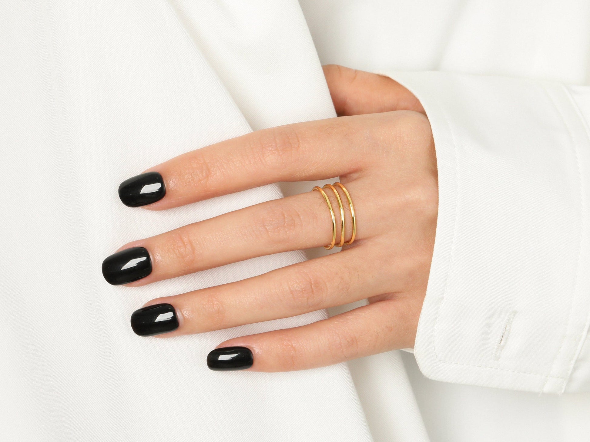 Hand with black nail polish wearing a gold ring on a white background
