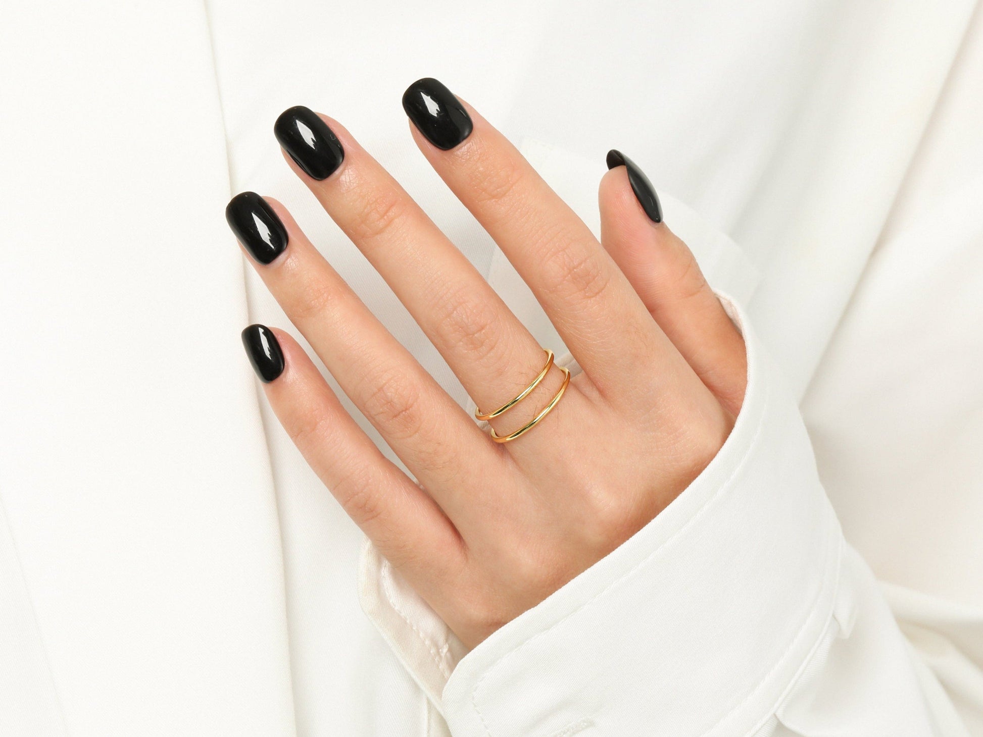 Hand with black nail polish wearing a gold ring on a white background