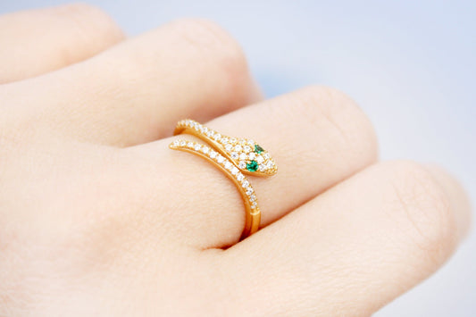 Gold ring with green gemstones on a finger against a light background
