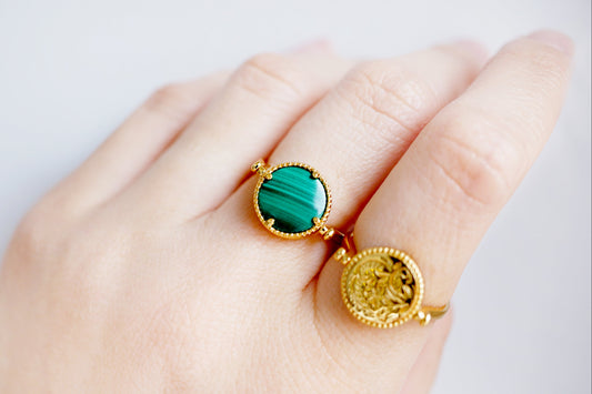 Gold rings with green gemstones on a hand against a white background
