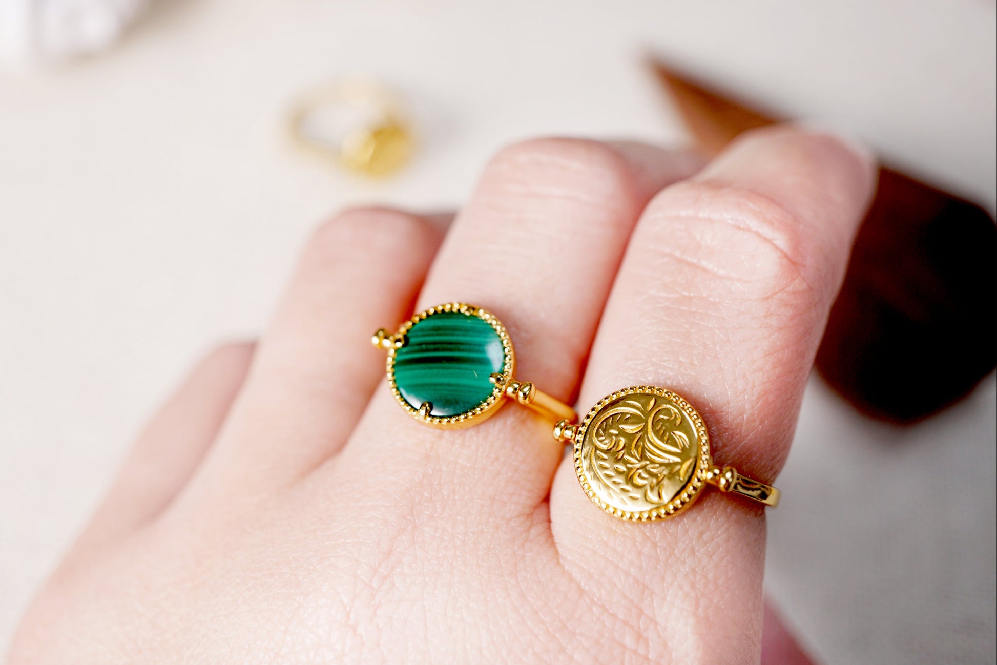 Gold ring with green gemstone on a hand against a neutral background