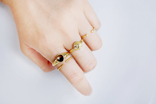 Hand wearing multiple gold rings with gemstones on a light background