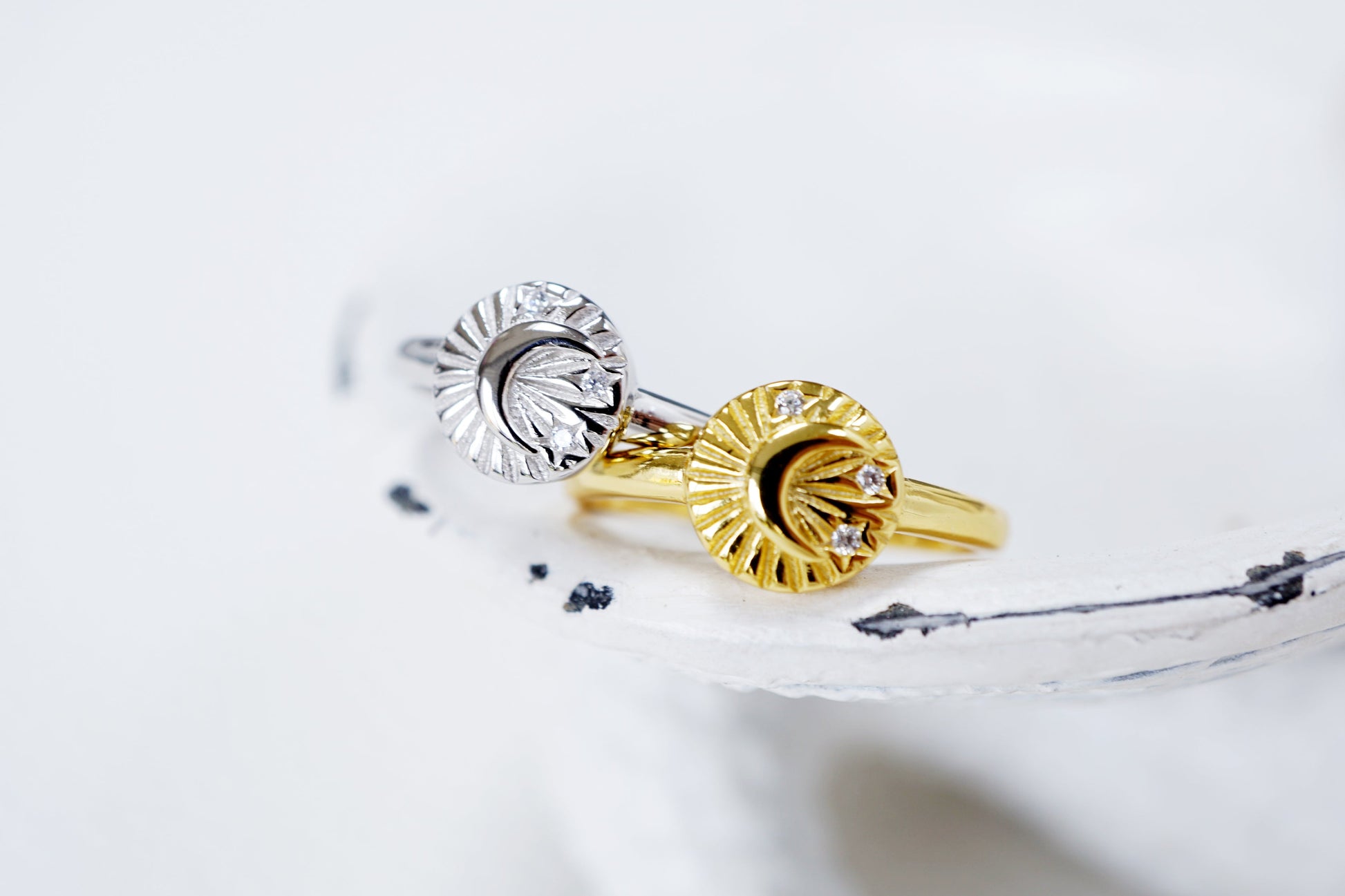 Two gold rings with sun and moon designs on a white surface