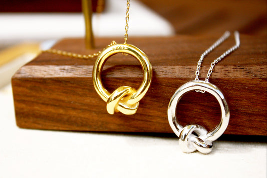 Gold and silver knot-shaped necklaces on a wooden stand.