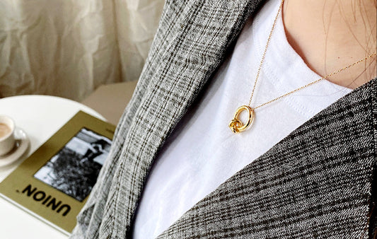 Person wearing a gold necklace with a blurred background of a coffee cup and book.