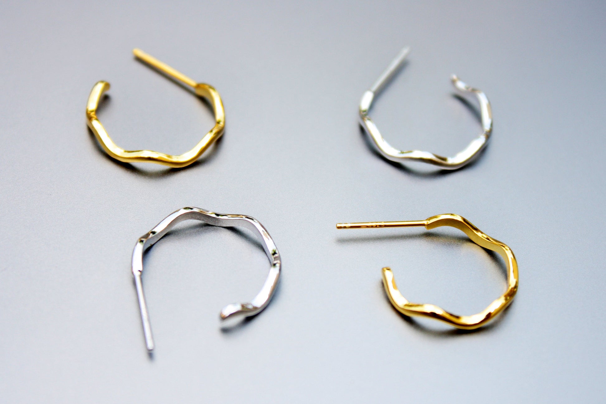 Four pairs of hoop earrings in gold and silver on a light gray background