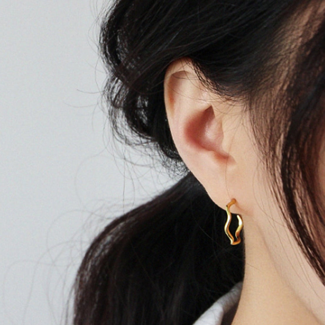 Close-up of a person wearing a gold hoop earring against a plain background