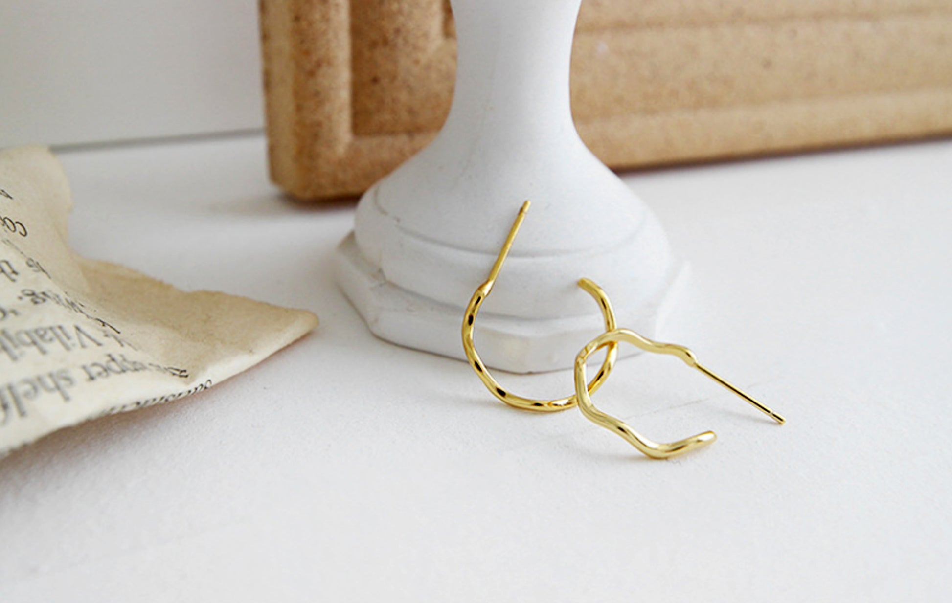 Gold earrings on a white surface with a neutral background
