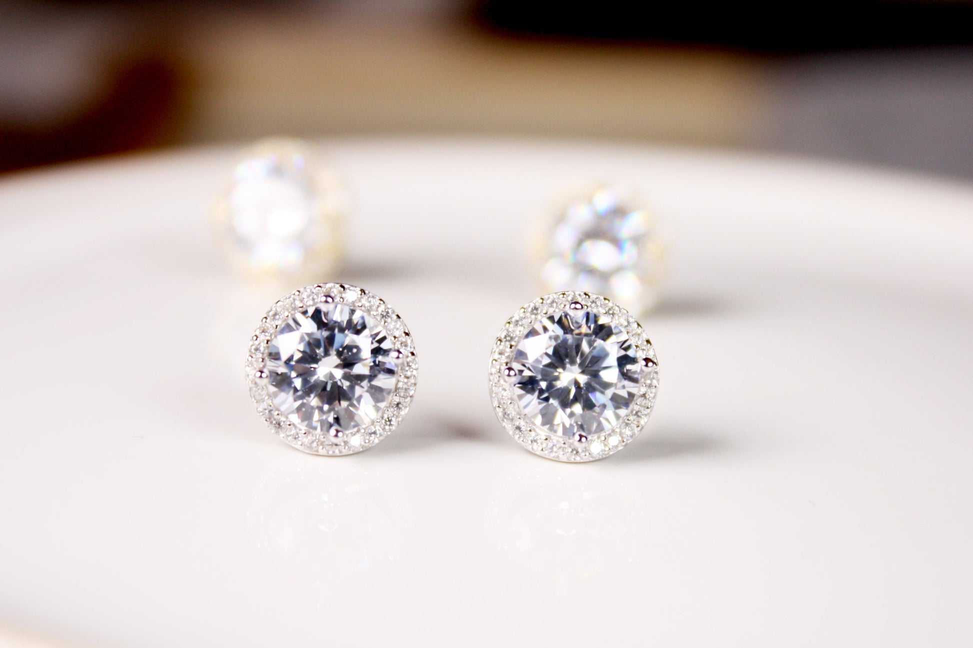 Pair of diamond stud earrings on a white surface with a blurred background