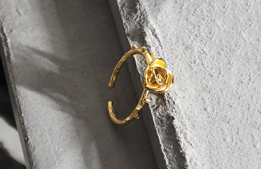 Gold ring with a rose design on a textured gray surface