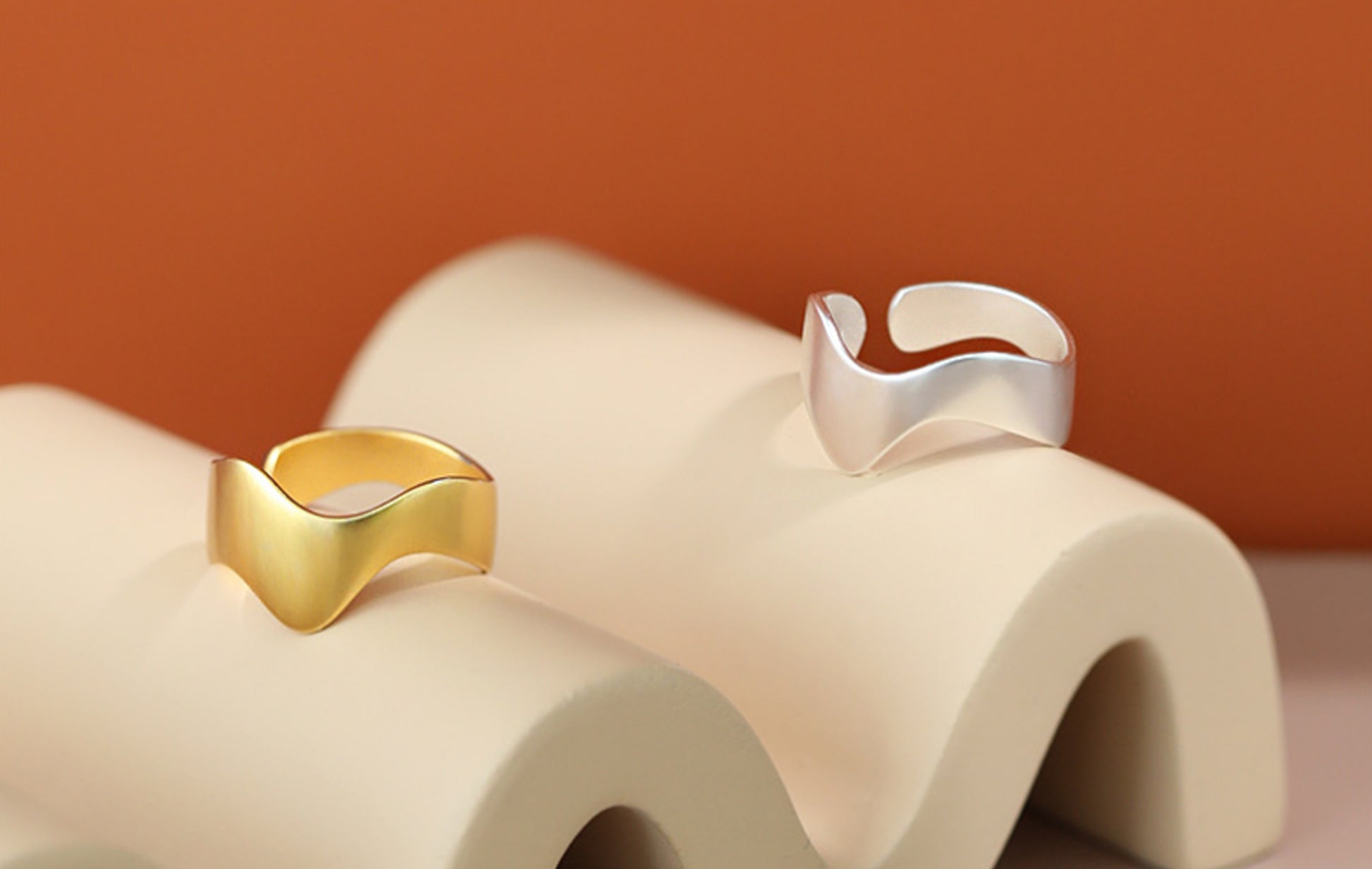Gold and silver rings on a textured beige surface with a warm brown background