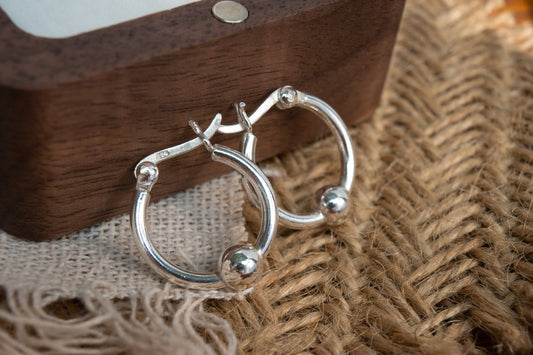 Silver hoop earrings on a textured fabric surface with a wooden box in the background