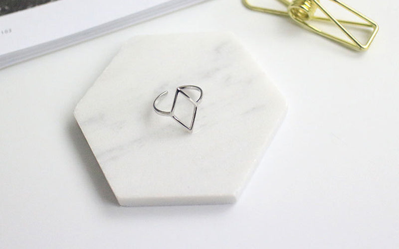 Silver ring on a hexagonal marble jewelry dish with a gold clip in the background.