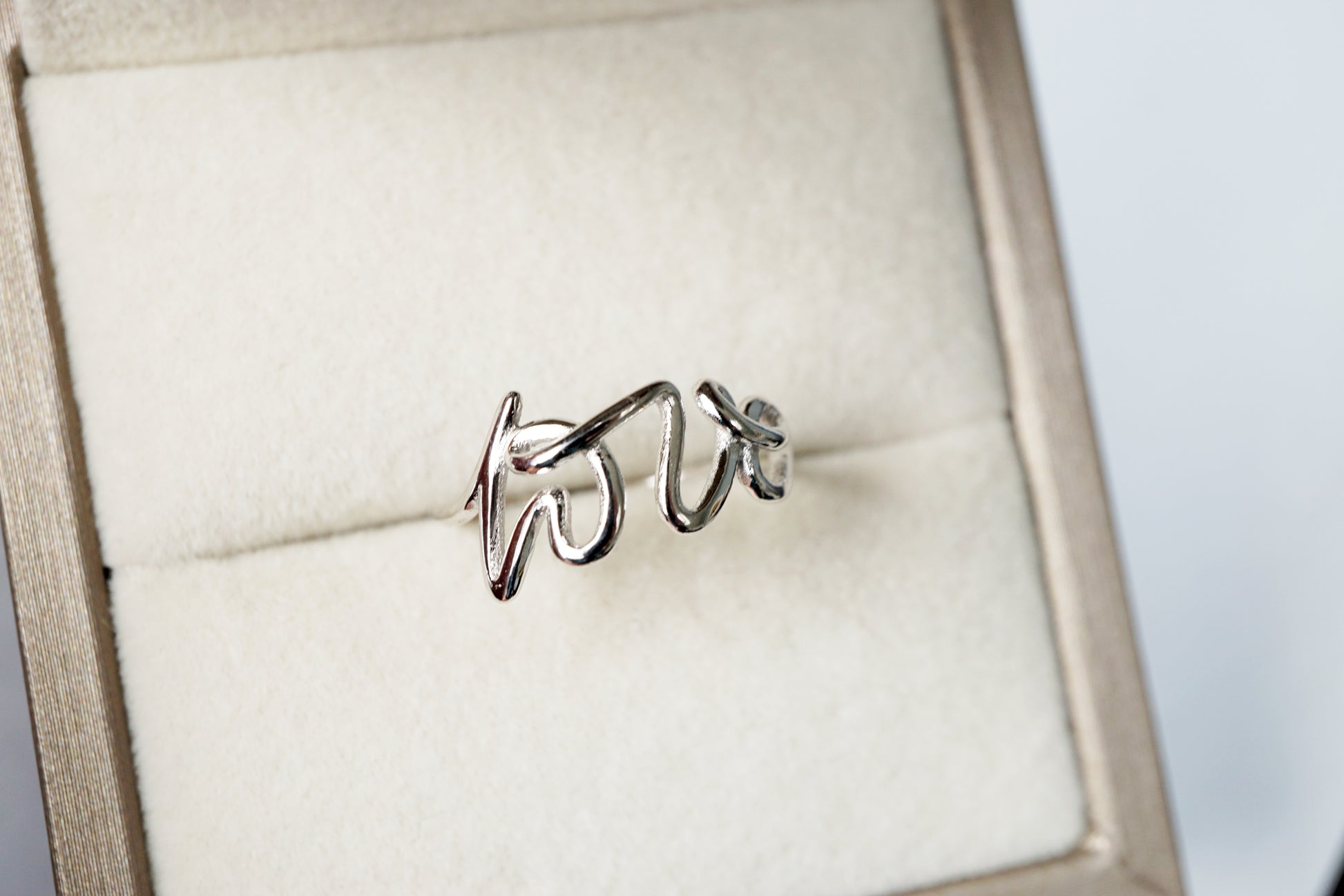 Silver ring with 'LOVE' engraving on a beige cushioned jewelry box