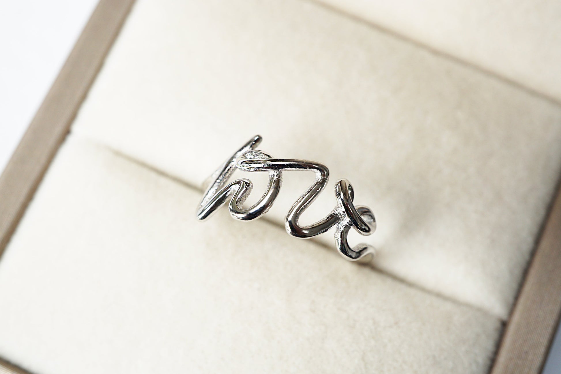 Silver ring with 'love' engraving on a white cushioned stand