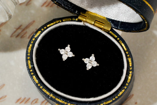 Pair of diamond earrings in a black and gold jewelry box on an old letter background