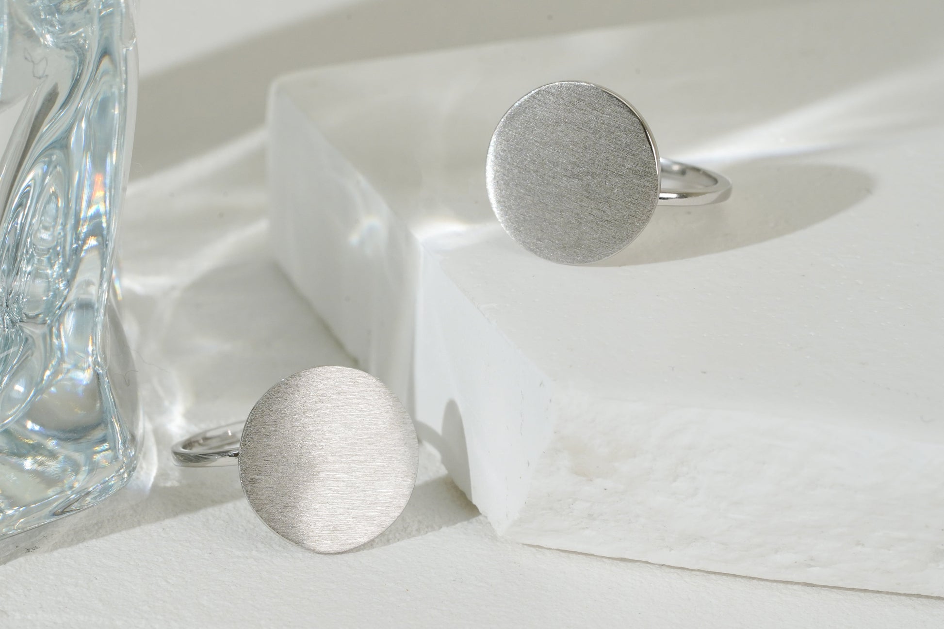 Silver ring and earrings on a white surface with a glass object in the background