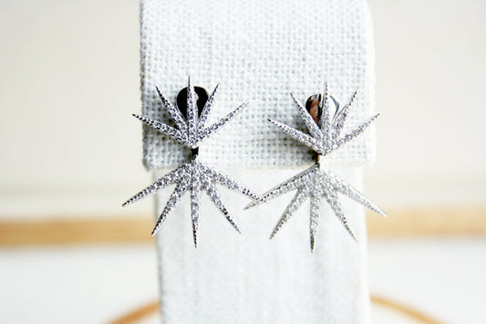 Silver starburst earrings on a white cushion with a blurred background