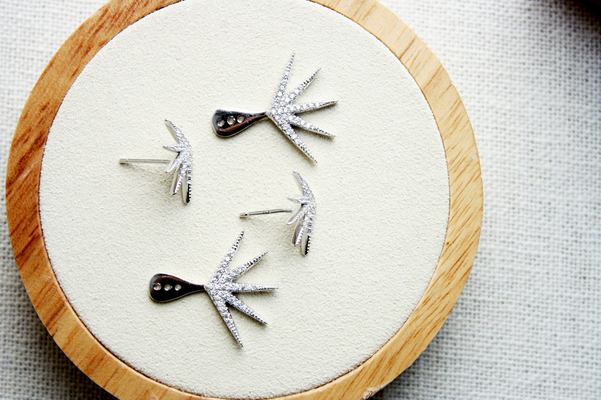 Set of earrings on a circular wooden stand with a white cloth background