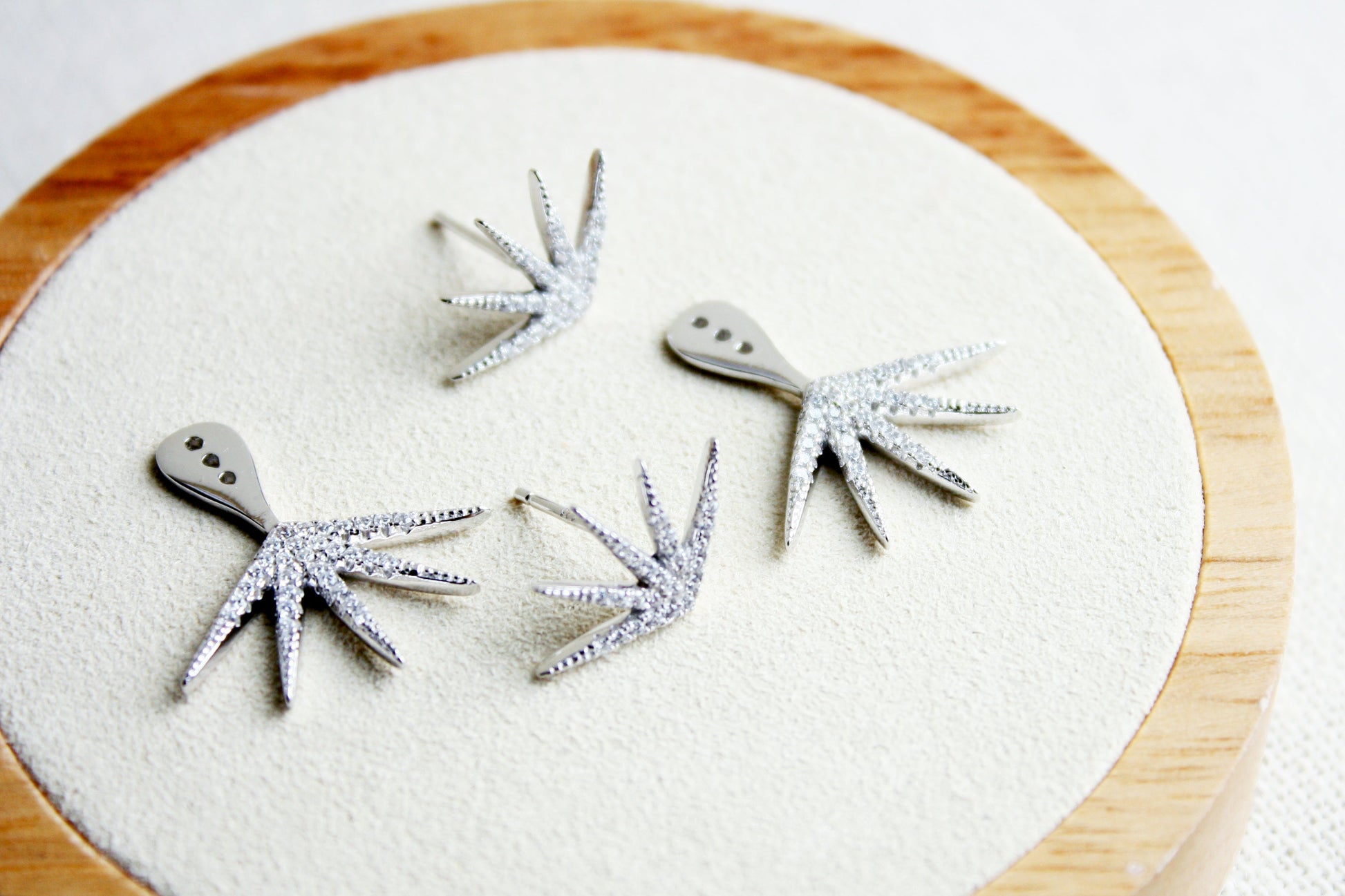 Silver bird-shaped earrings on a round wooden platform with a white background