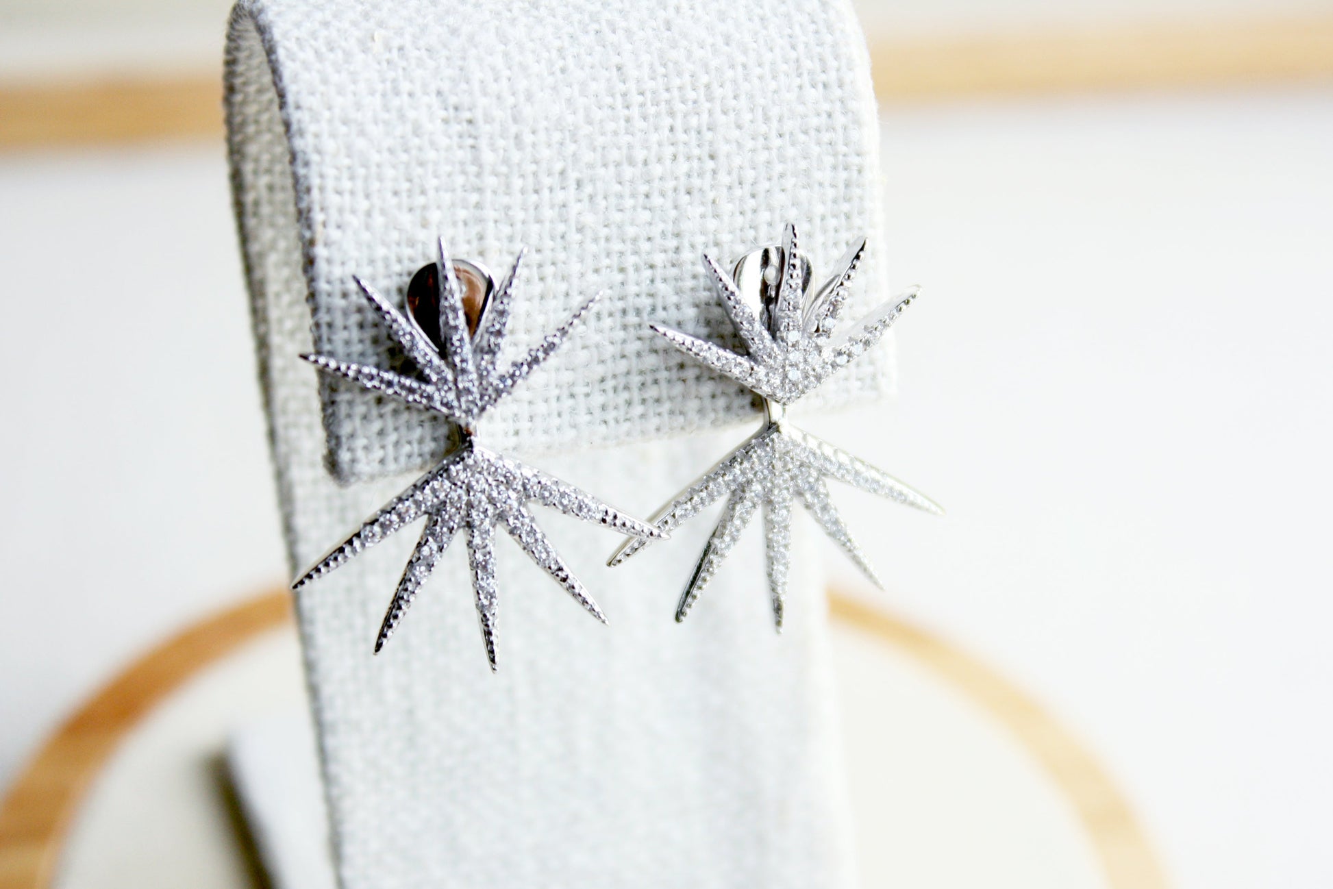 Pair of silver star-shaped earrings on a white cloth with a wooden surface underneath.