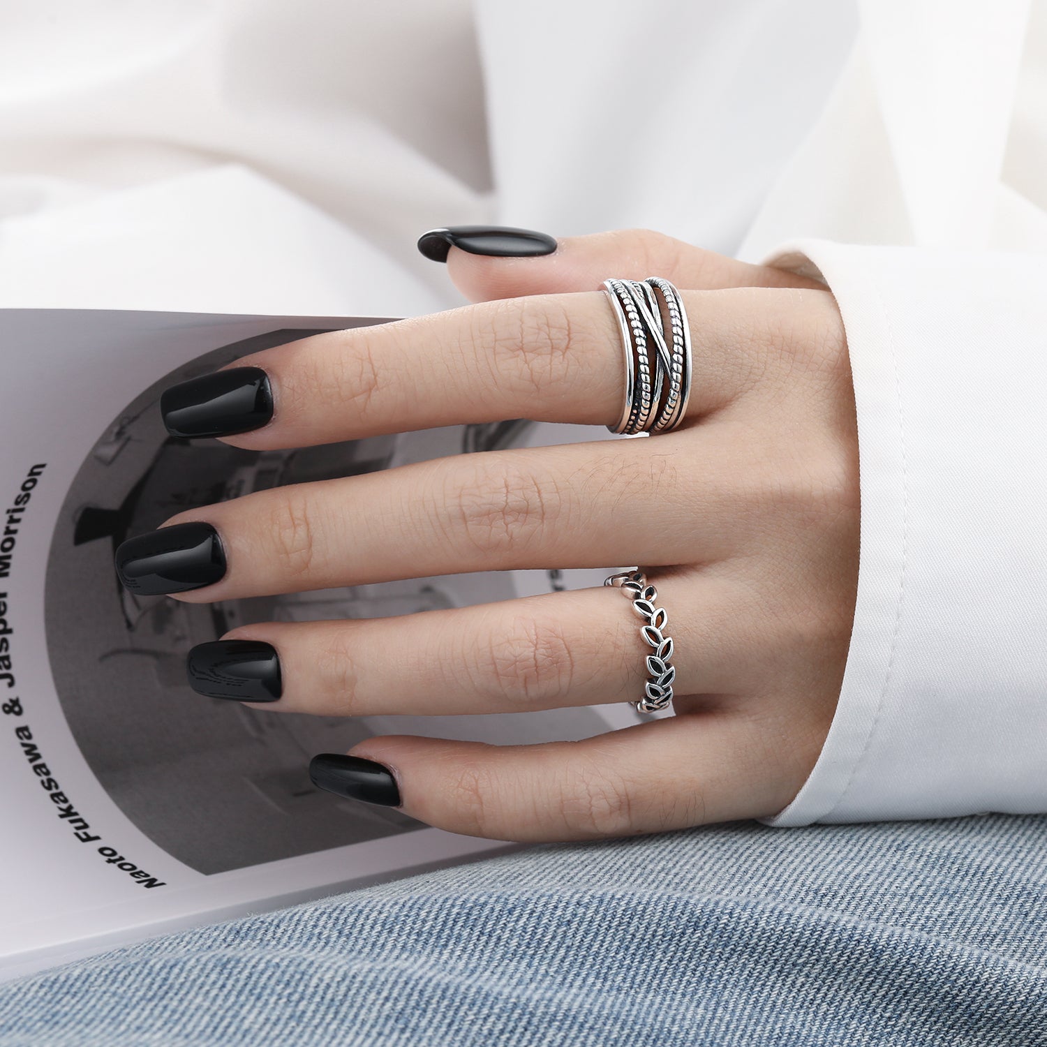 Hand with black nail polish wearing multiple rings on a book background