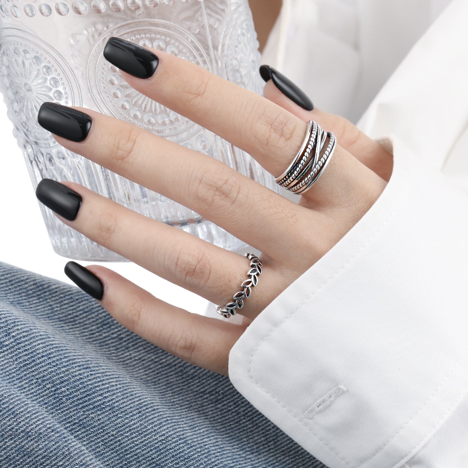 Hand with black nail polish wearing multiple rings on a blurred background