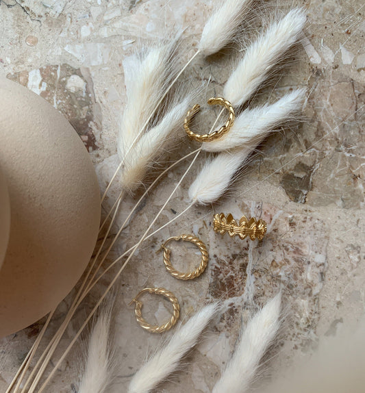 Gold hoop earrings on a textured surface with dried white grasses