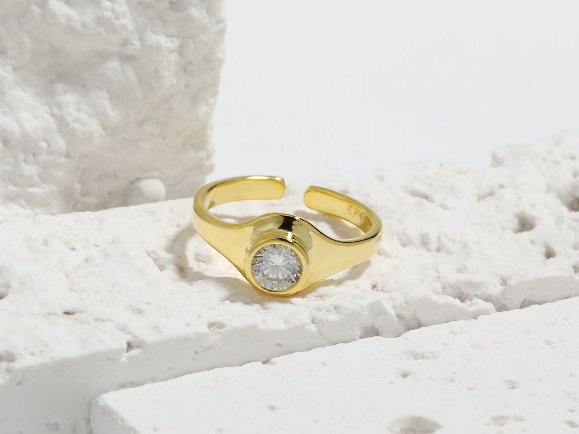 Gold ring with a diamond on a textured white surface