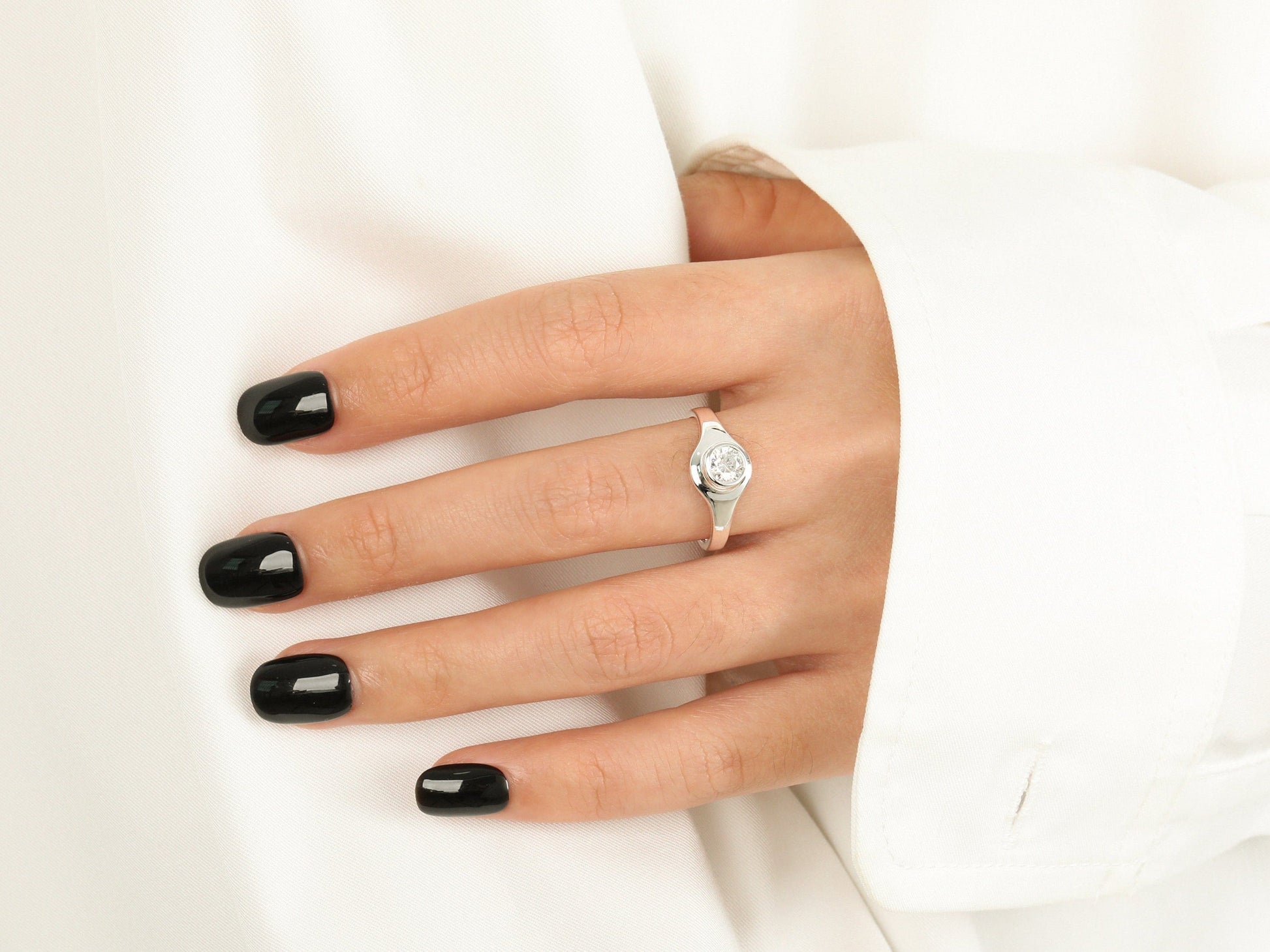 Hand with black nail polish wearing a diamond ring on a white background