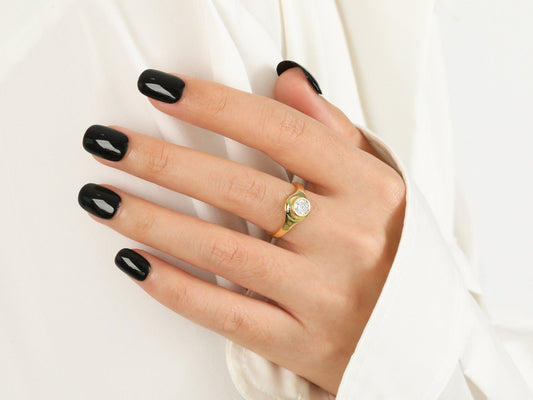 Hand with black nail polish wearing a gold ring on a white background