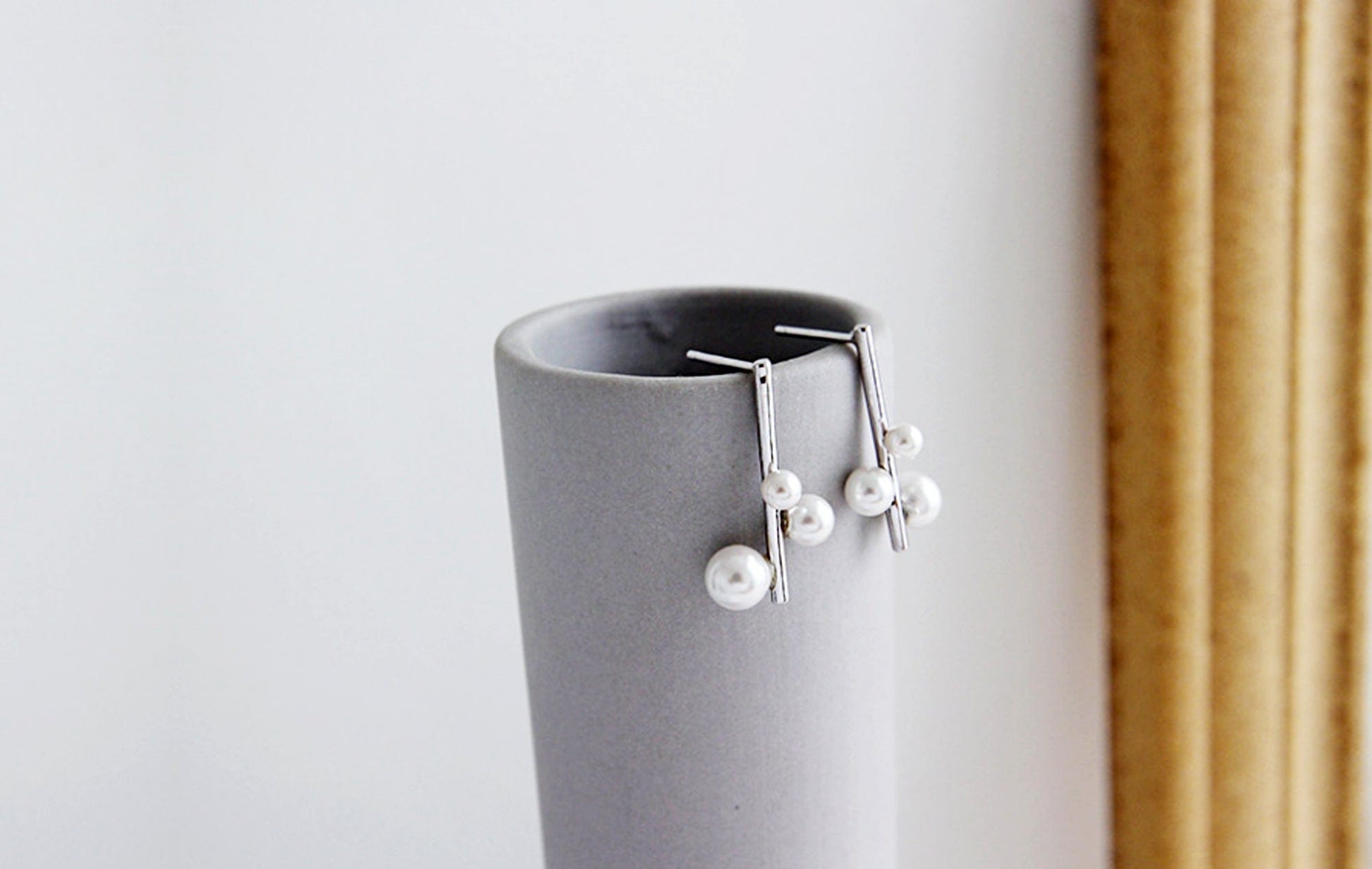 Silver earrings with pearls on a gray stand against a white background
