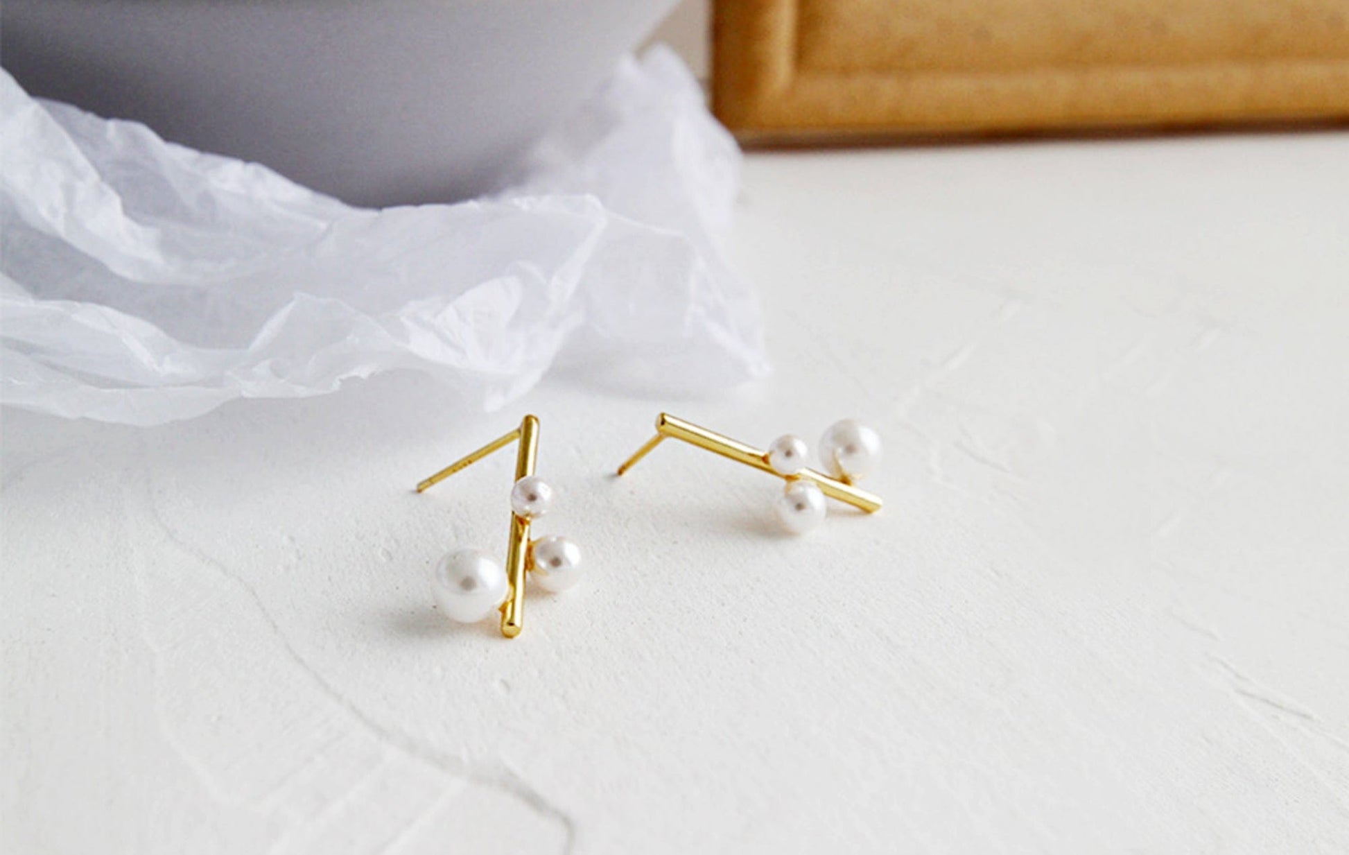 Gold earrings with pearls on a white fabric background