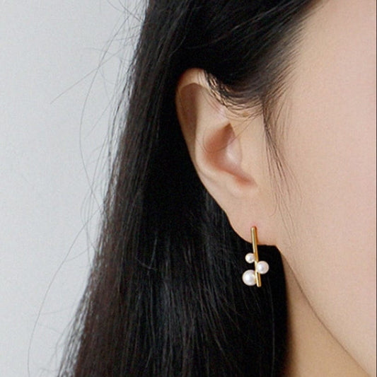 Close-up of a person wearing gold earrings with small pearls against a plain background