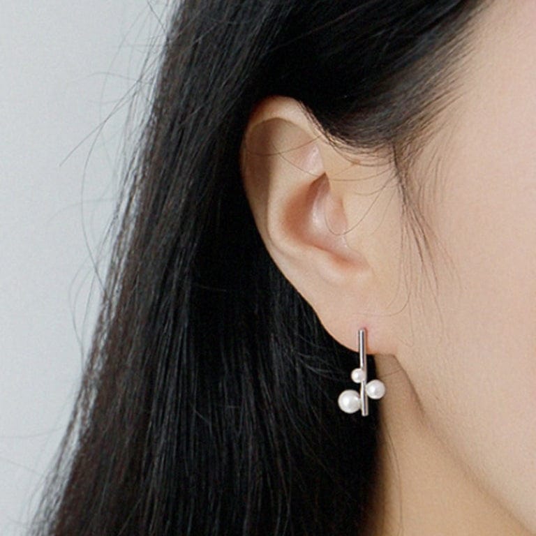 Close-up of an ear wearing a silver earring with three small pearls against a neutral background