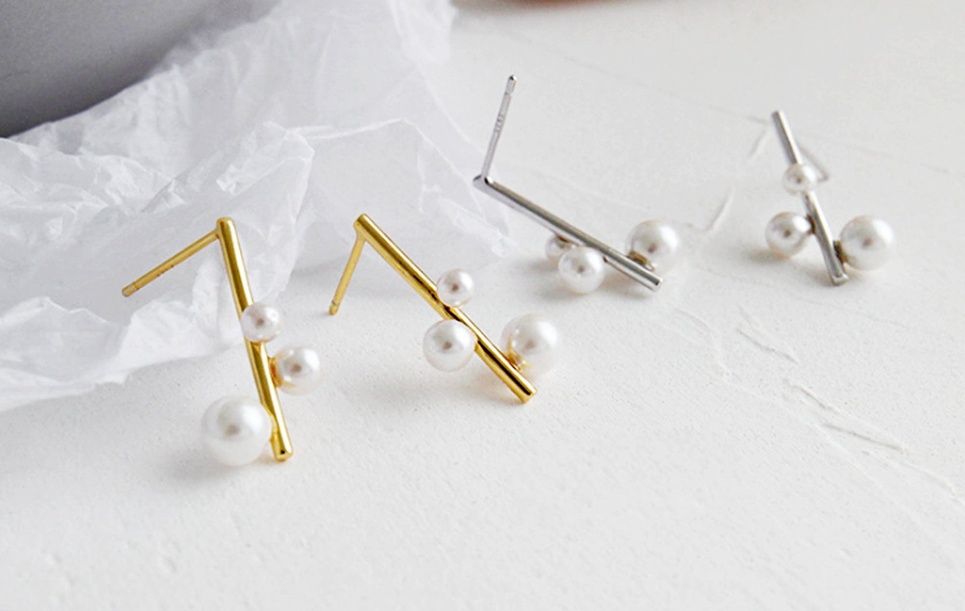 Gold and silver earrings with pearls on a light background