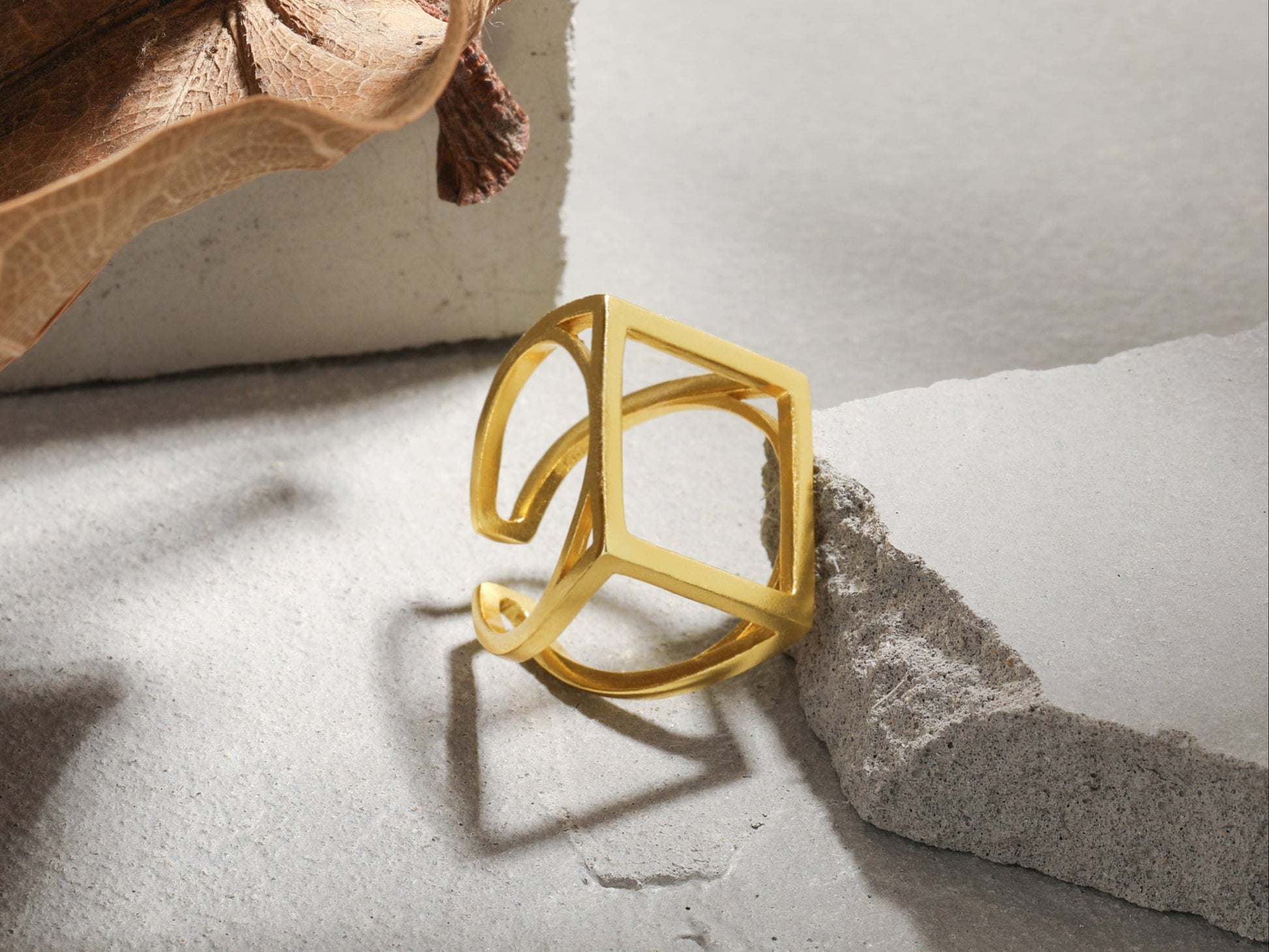 Gold geometric ring on a textured surface with a leaf