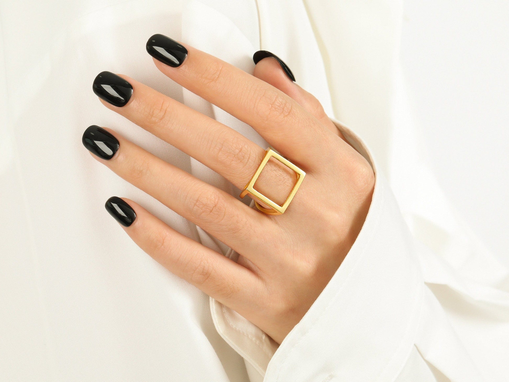 Hand wearing a gold ring with black nail polish on a white background