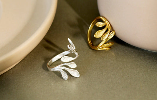 Two leaf-shaped rings, one silver and one gold, on a neutral background.